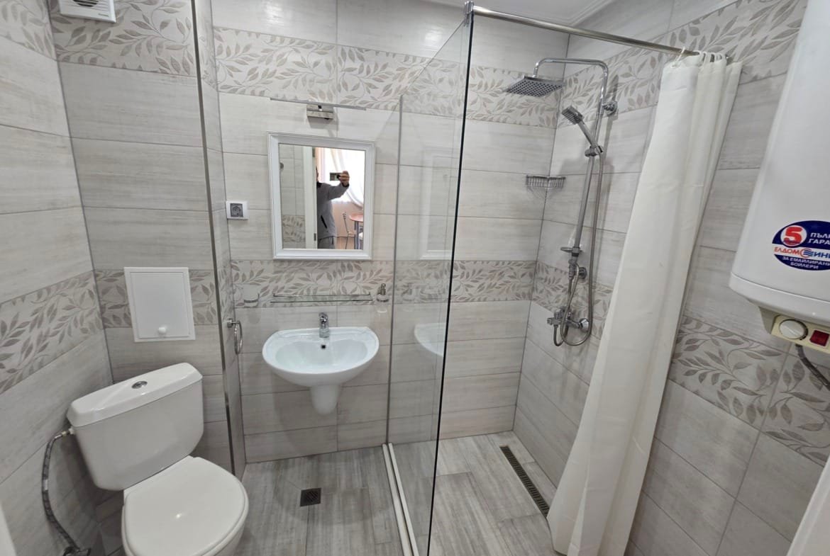 Современная ванная комната с душевой кабиной, унитазом и раковиной, отделанная плиткой в нейтральных тонах.