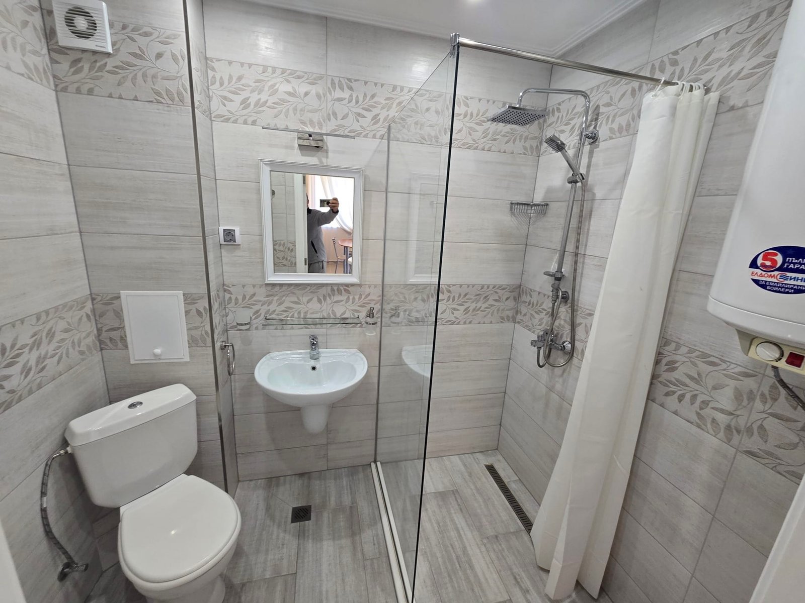 Современная ванная комната с душевой кабиной, унитазом и раковиной, отделанная плиткой в нейтральных тонах.