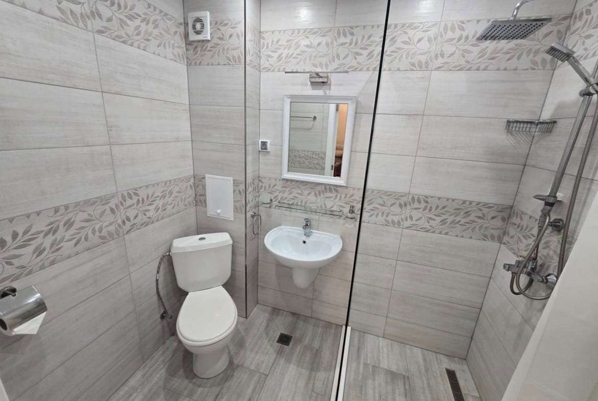 Современная ванная комната с плиткой, душевой кабиной, унитазом и раковиной, идеальна для покупки недвижимости в Болгарии.