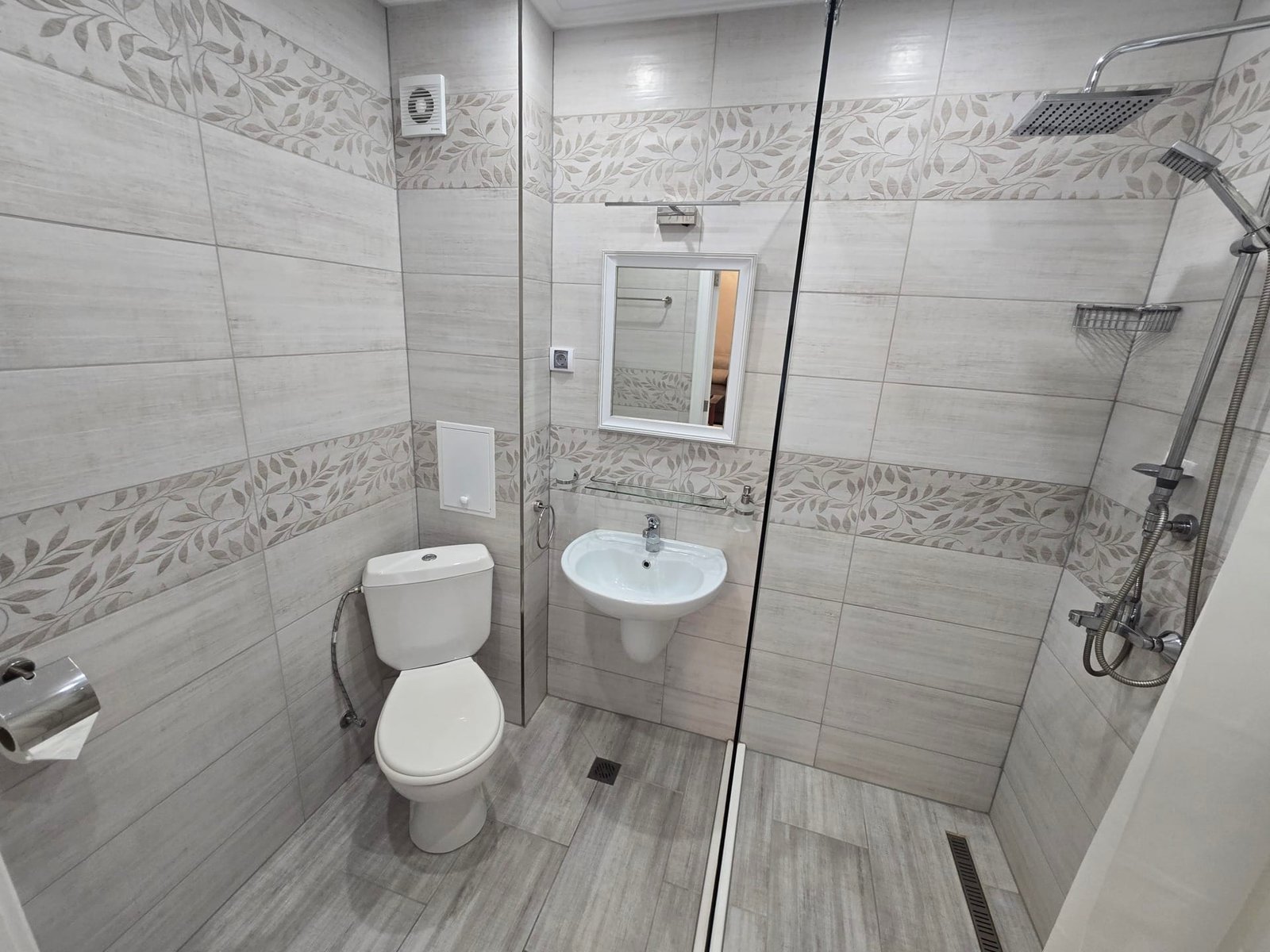 Современная ванная комната с плиткой, душевой кабиной, унитазом и раковиной, идеальна для покупки недвижимости в Болгарии.