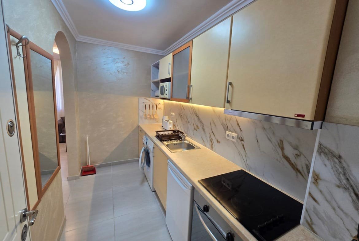 Современная кухня с плитой, духовым шкафом и холодильником. Светлые тона, мраморная отделка, подходит для покупки недвижимости в Болгарии.