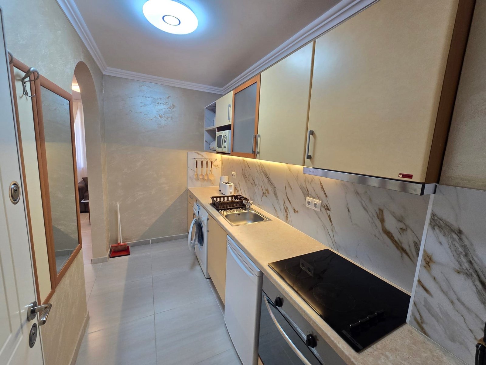 Современная кухня с плитой, духовым шкафом и холодильником. Светлые тона, мраморная отделка, подходит для покупки недвижимости в Болгарии.