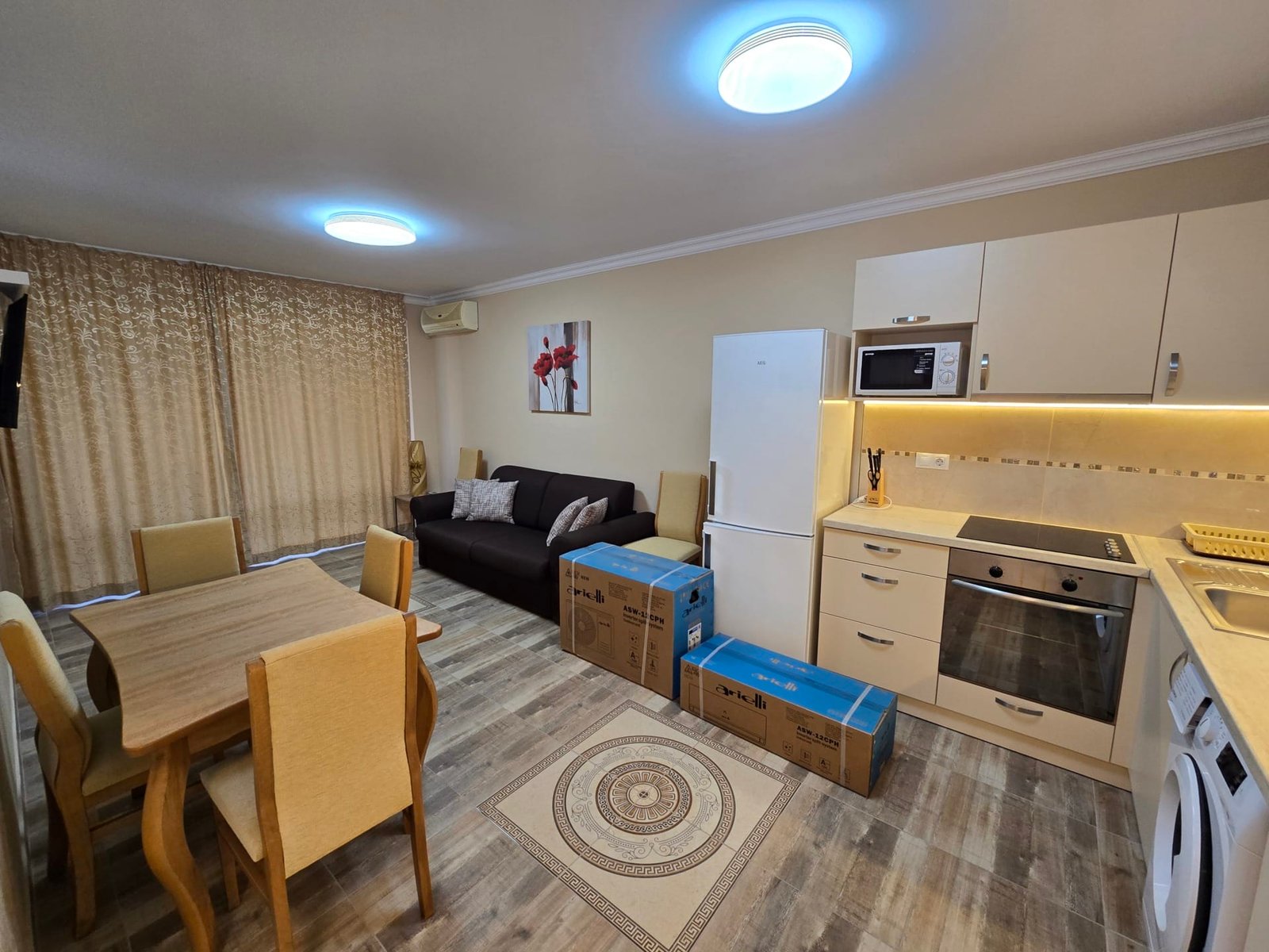 Современная кухня-гостиная в Болгарии с новыми мебелью и бытовой техникой, готовая к продаже. Коробки и стол создают уют.