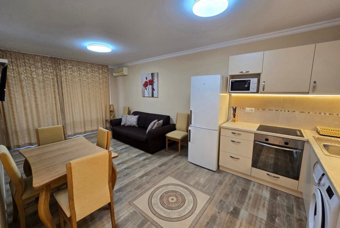 Современная кухня-студия с уютной мебелью, обеденным столом и бытовой техникой, подходящая для продажи недвижимости в Болгарии.