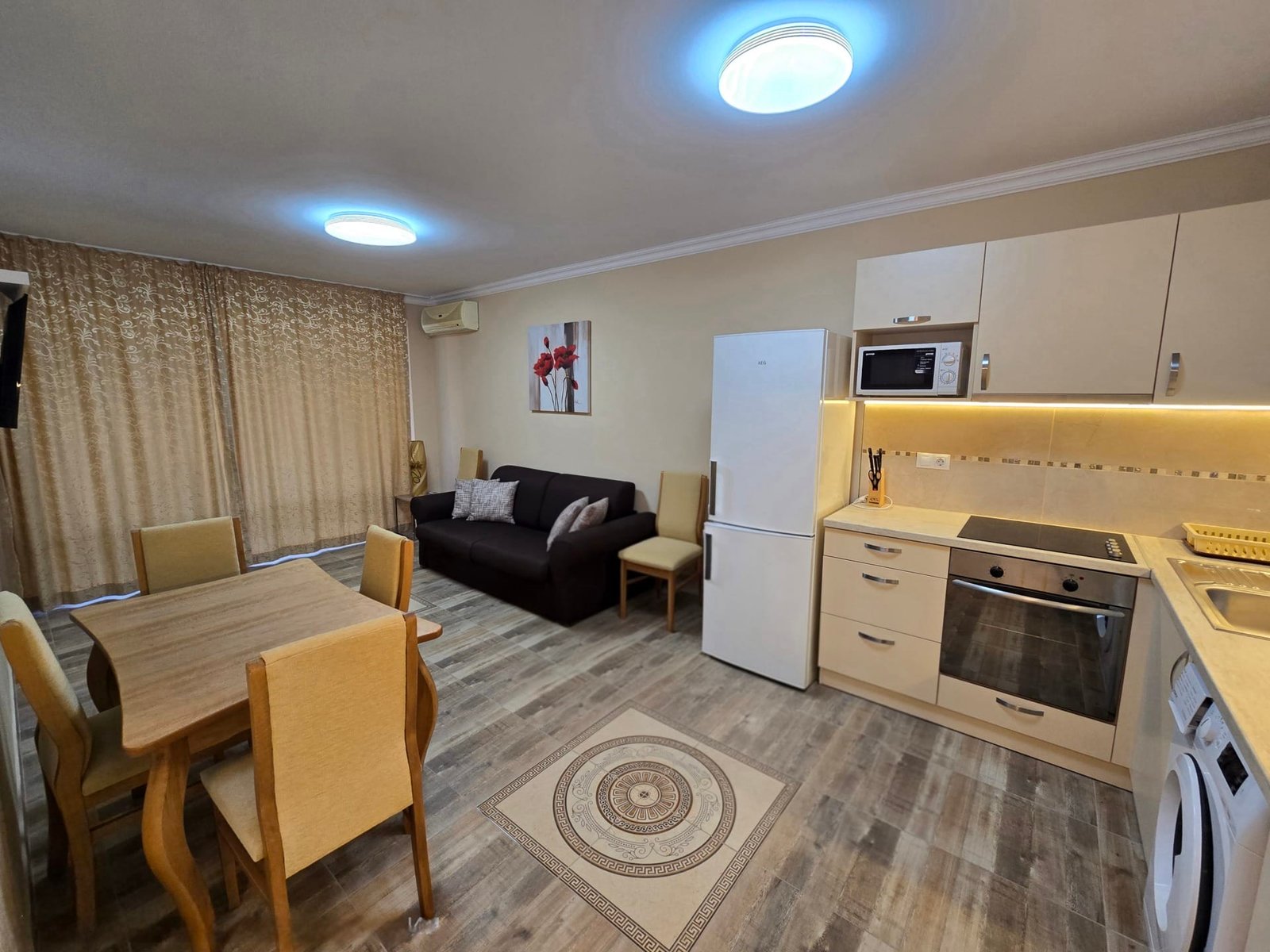 Современная кухня-студия с уютной мебелью, обеденным столом и бытовой техникой, подходящая для продажи недвижимости в Болгарии.