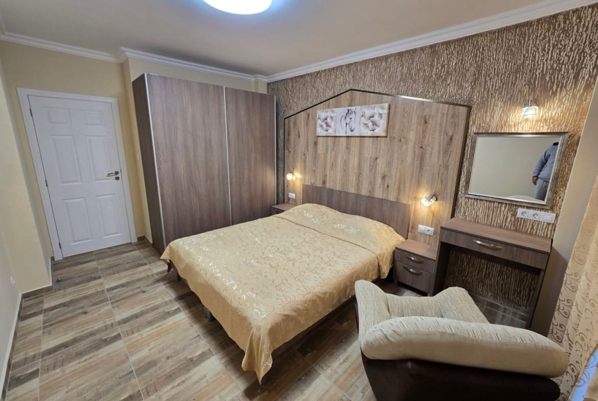 Уютная спальня с двуспальной кроватью, стеной из декоративной плитки и комодом, идеальна для покупки недвижимости в Болгарии.