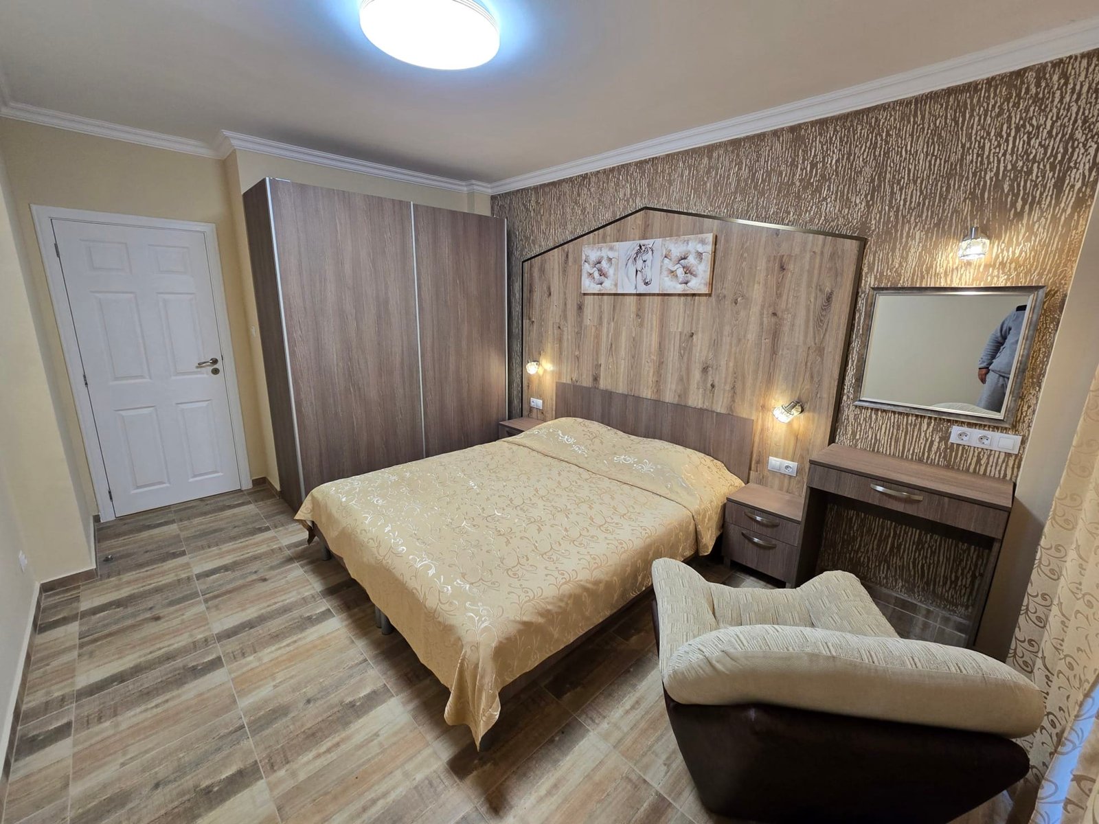 Уютная спальня с двуспальной кроватью, стеной из декоративной плитки и комодом, идеальна для покупки недвижимости в Болгарии.