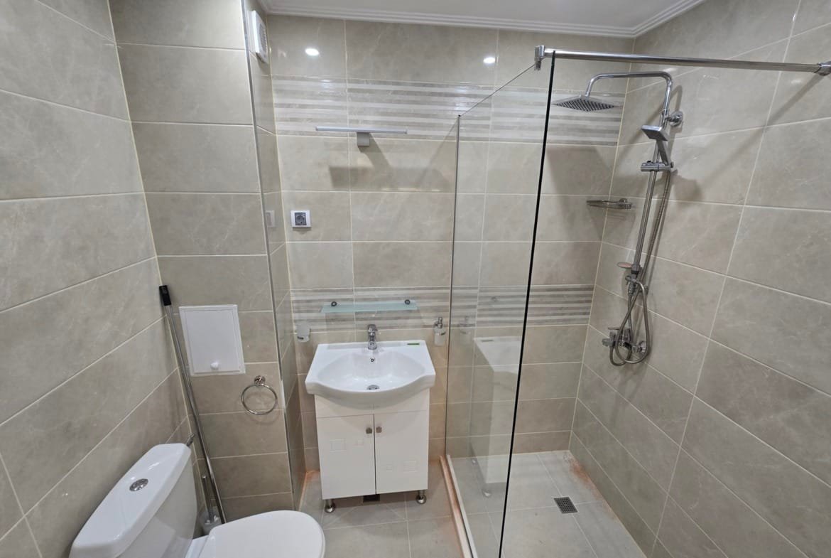 Современная ванная комната с душевой кабиной, умывальником и туалетом, оформленная в светлых тонах для продажи недвижимости в Болгарии.