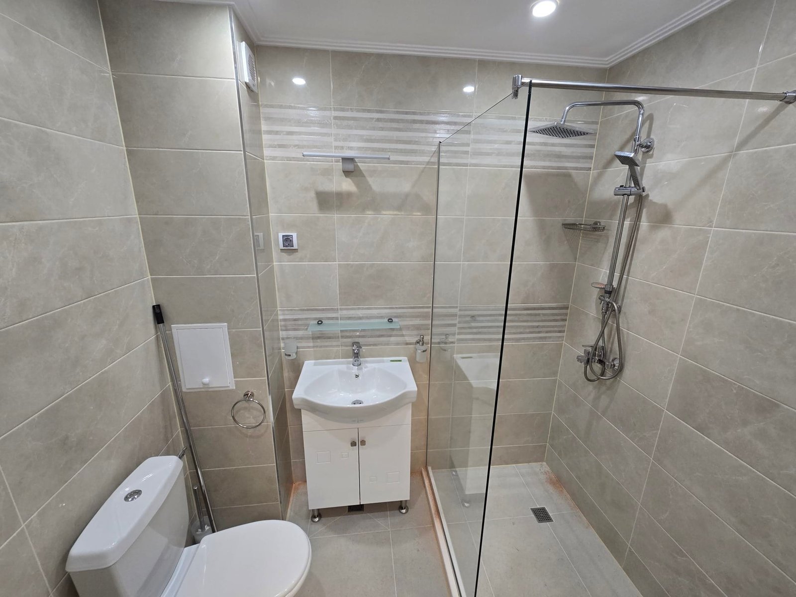 Современная ванная комната с душевой кабиной, умывальником и туалетом, оформленная в светлых тонах для продажи недвижимости в Болгарии.