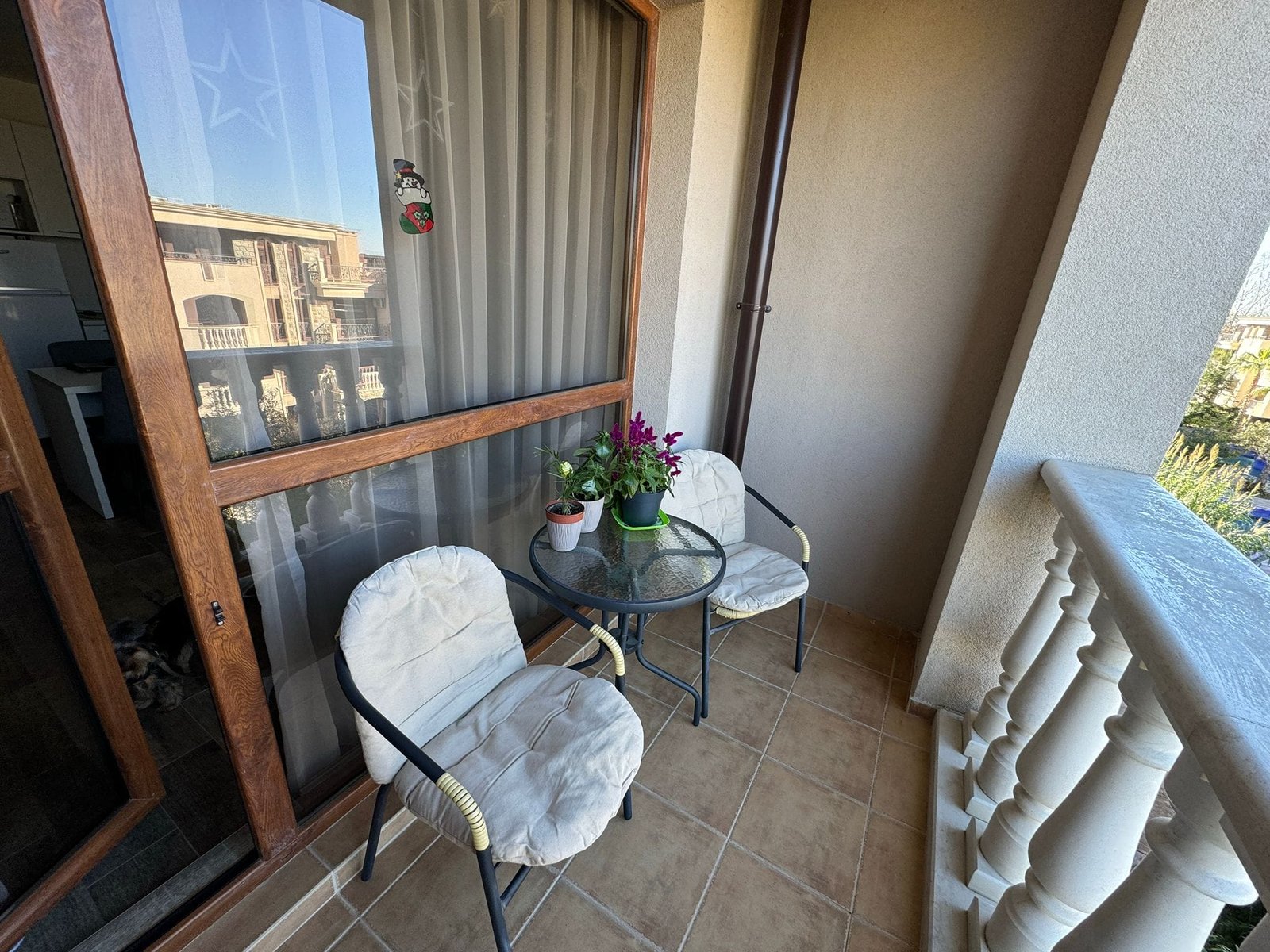 Уютный балкон с цветами и креслами для отдыха. Балкон с двумя креслами и столиком, цветами в горшке и видом на окружающий ландшафт, идеален для продажи недвижимости в Болгарии.