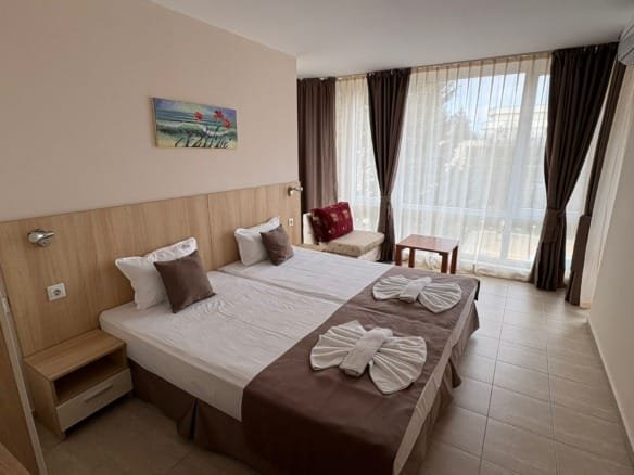 Современный номер в гостинице с двумя кроватями, светлым интерьером и большим окном, идеально для отдыха в Болгарии.