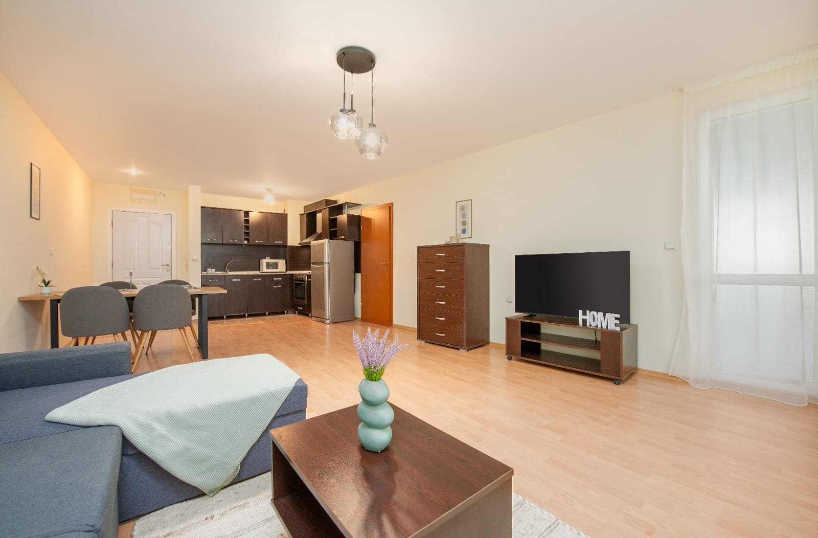 Современная квартира в Болгарии с уютной гостиной, кухней и телевизором, идеальна для проживания или аренды.