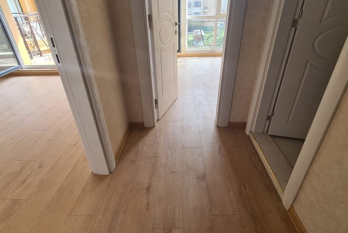 Светлый коридор новой квартиры с деревянным полом и дверями, ведущими в комнаты, идеально подходит для продажи недвижимости в Болгарии.