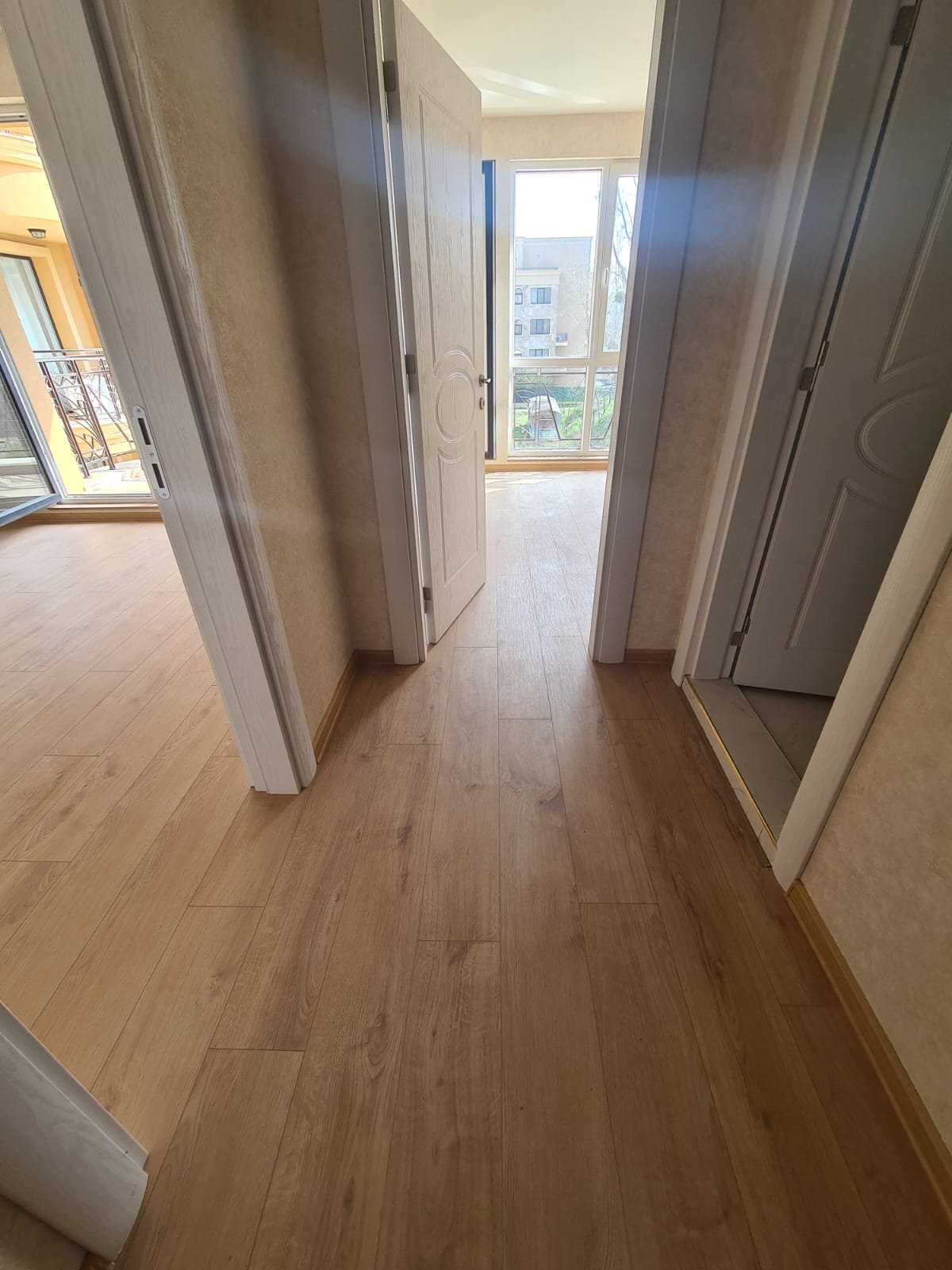 Светлый коридор новой квартиры с деревянным полом и дверями, ведущими в комнаты, идеально подходит для продажи недвижимости в Болгарии.