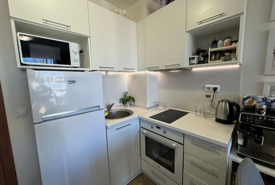 Современная кухня с белыми шкафами, встроенной техникой и компактной планировкой, подходящая для жилья в Болгарии.