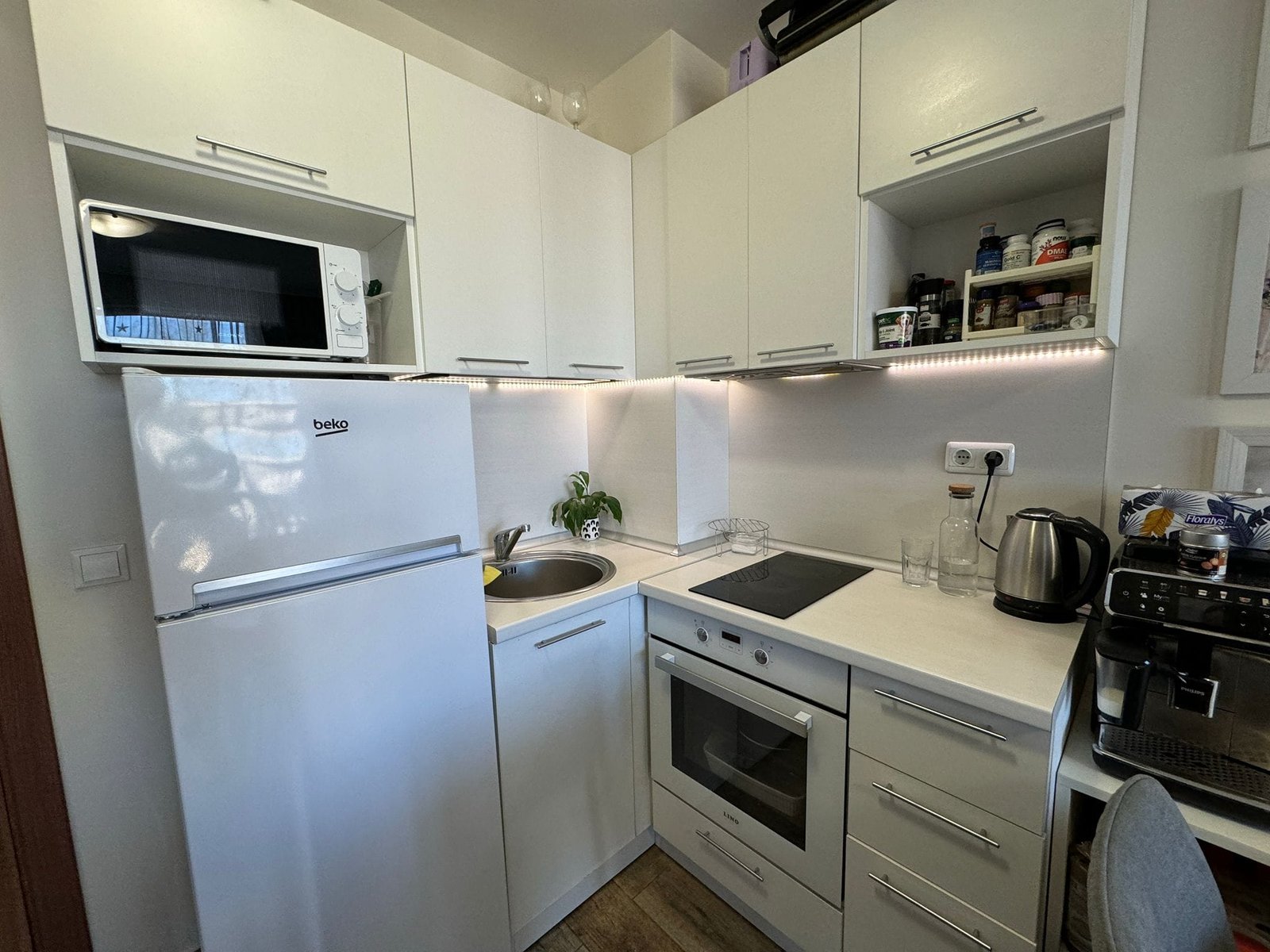 Современная кухня с бытовой техникой и светлыми фасадами Современная кухня с белыми шкафами, встроенной техникой и компактной планировкой, подходящая для жилья в Болгарии.