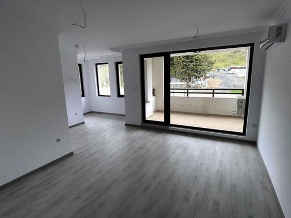 Современная квартира в Болгарии с открытой планировкой, светлыми стенами и большими окнами, ведущими на балкон.