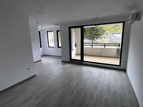 Современная квартира в Болгарии с открытой планировкой, светлыми стенами и большими окнами, ведущими на балкон.