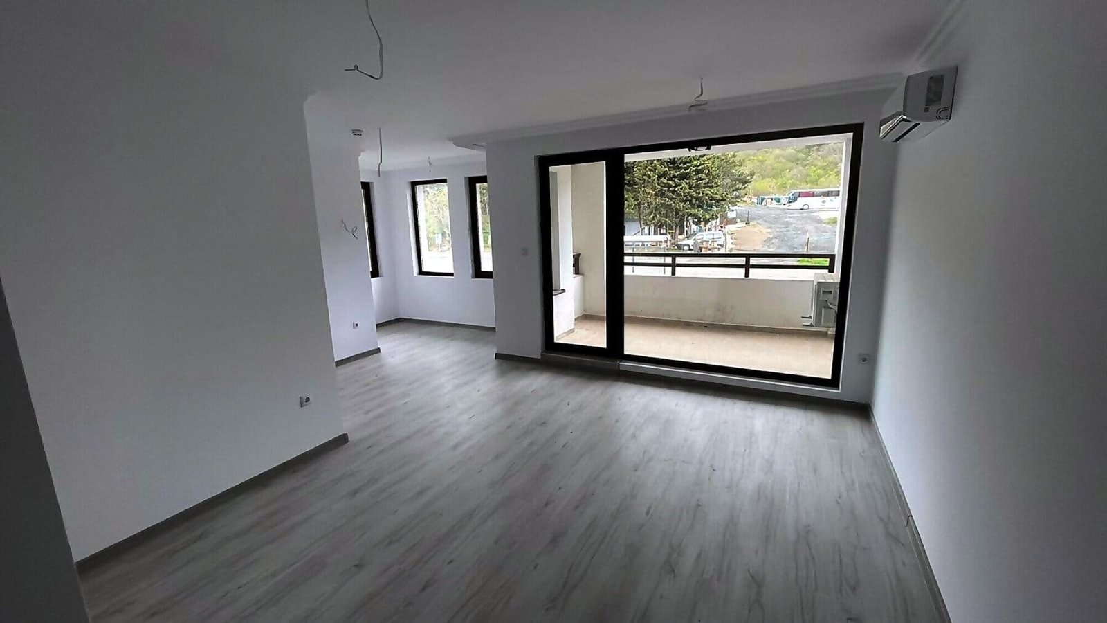 Современная квартира в Болгарии с открытой планировкой, светлыми стенами и большими окнами, ведущими на балкон.