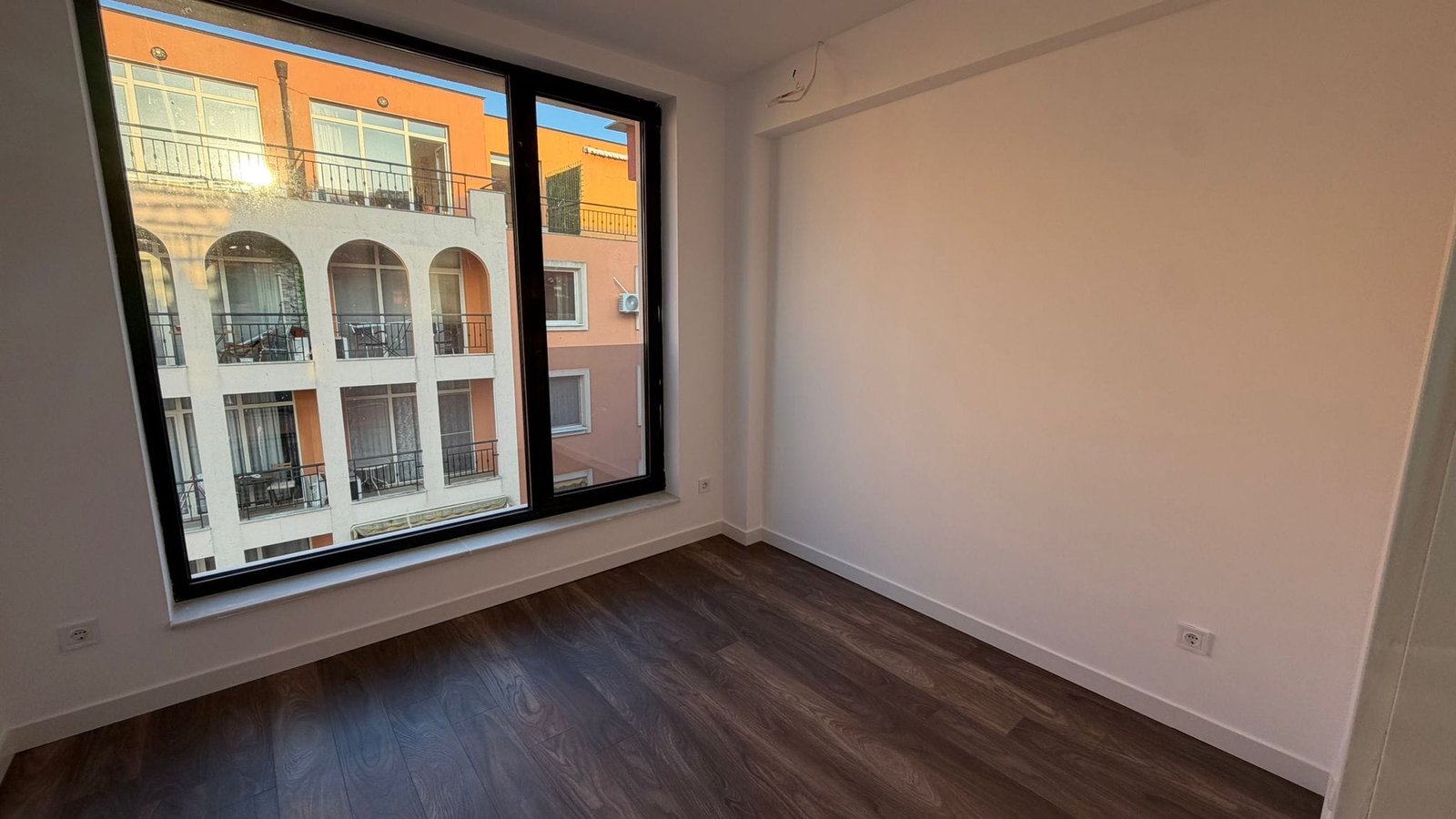 Современный интерьер квартиры с большим окном и видом на улицу Современная комната с большим окном и видом на жилой комплекс в Болгарии, идеально подходящая для покупки недвижимости.