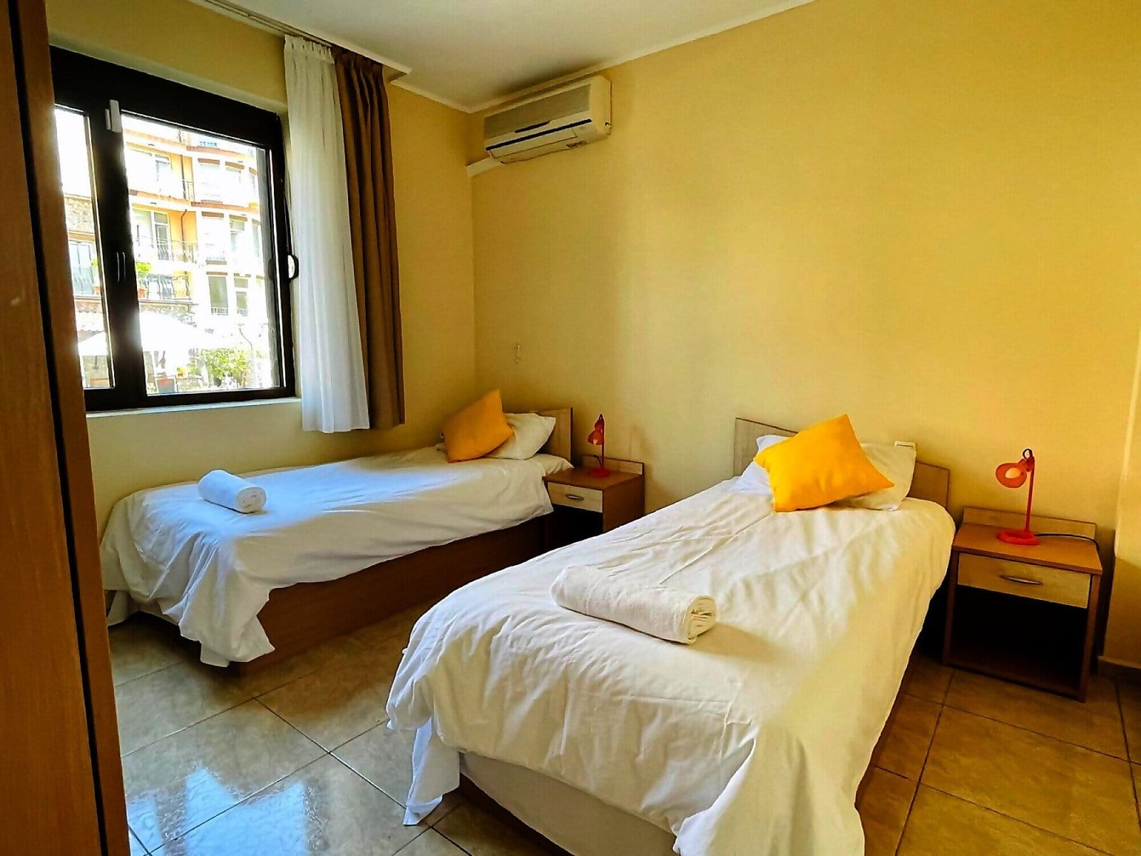 Современная спальня с двумя односпальными кроватями, светлыми стенами и акцентными подушками, идеальная для отдыха в Болгарии.