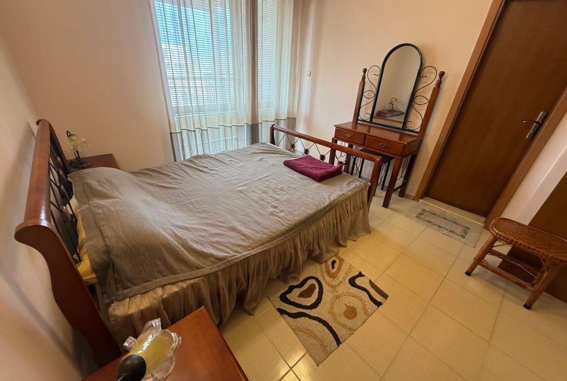 Уютная спальня с двойной кроватью, комодом и зеркалом, идеальна для продажи недвижимости в Болгарии.