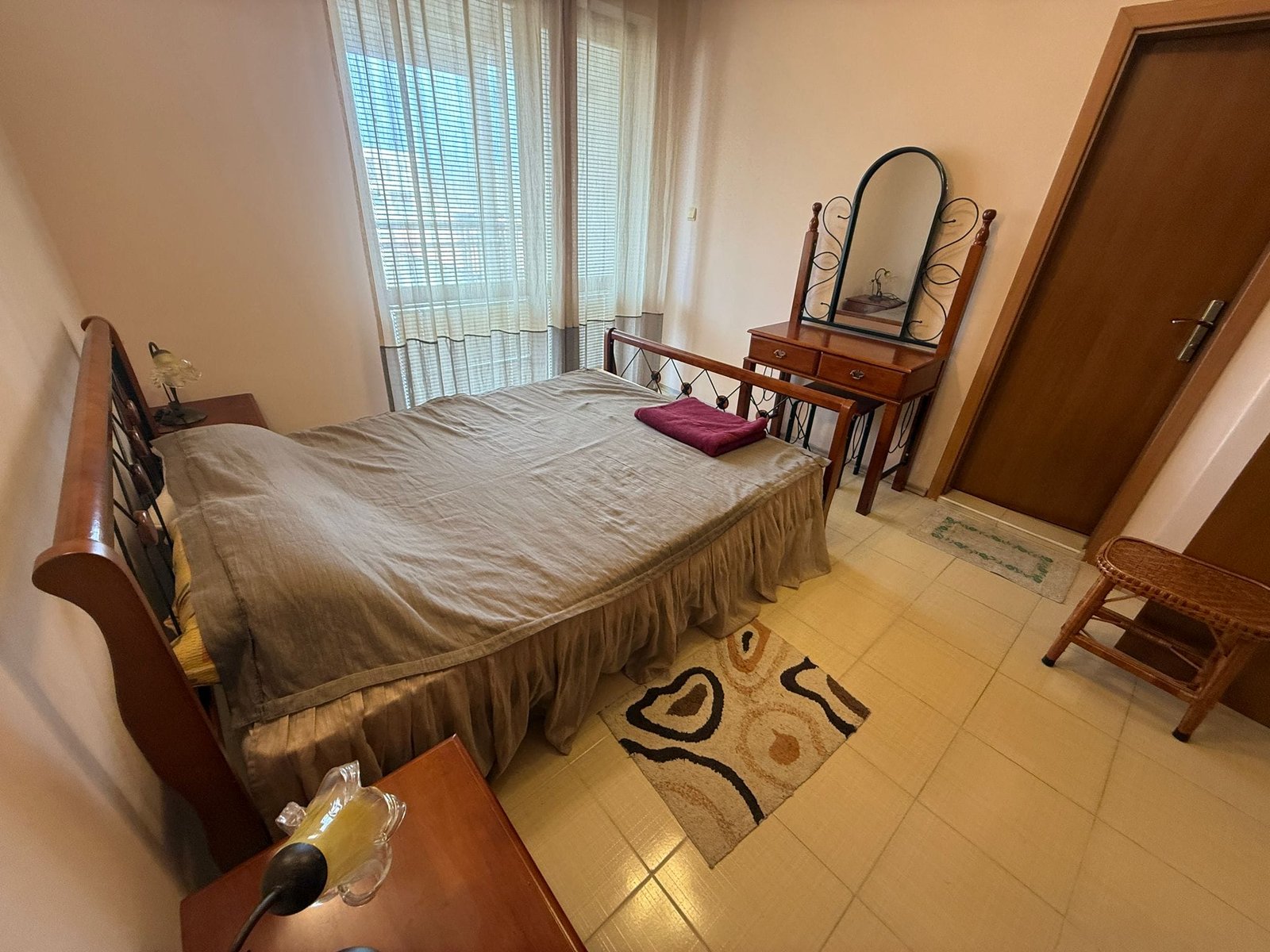 Уютная спальня с двойной кроватью, комодом и зеркалом, идеальна для продажи недвижимости в Болгарии.