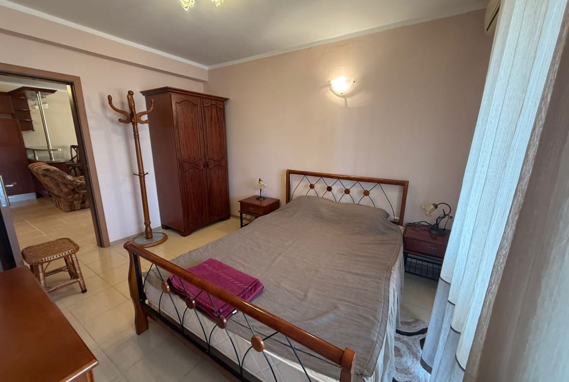 Современная спальня с кроватью и деревянной мебелью, светлые стены, уютная обстановка для продажи недвижимости в Болгарии.