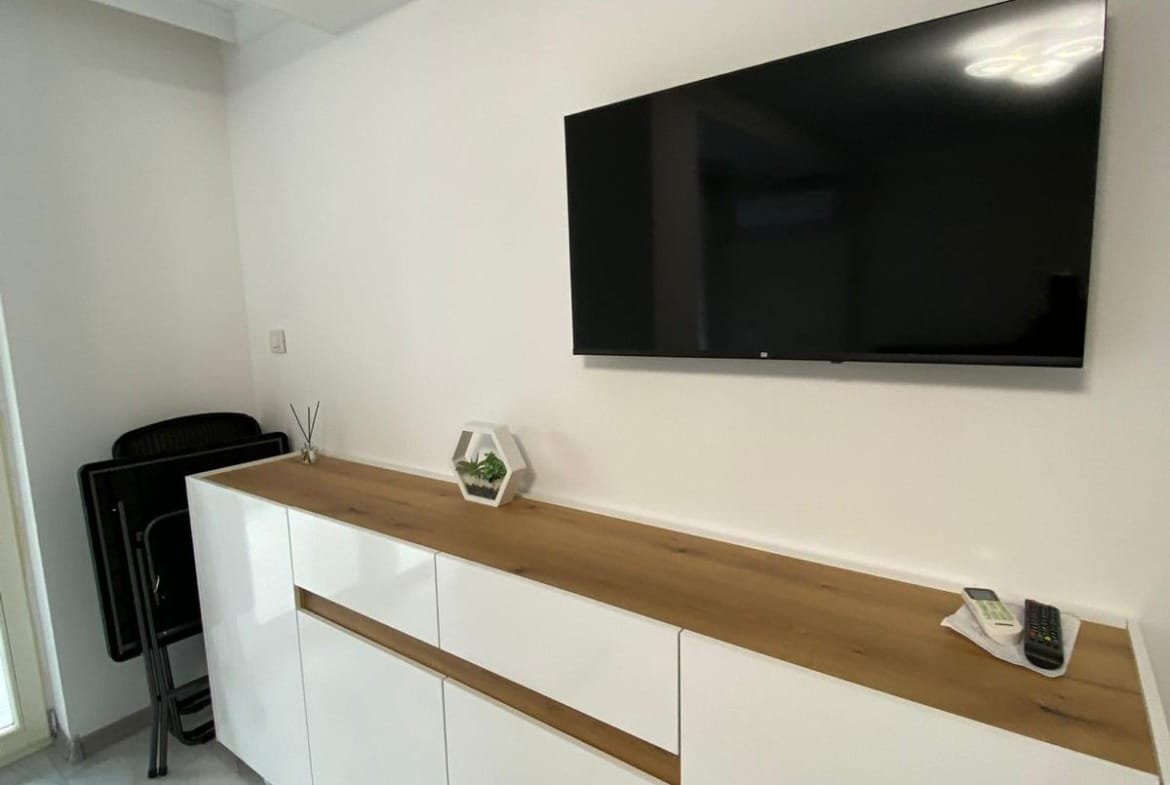 Современный интерьер квартиры в Болгарии с белым стендом и телевизором на стене, подходящим для сдачи в аренду.