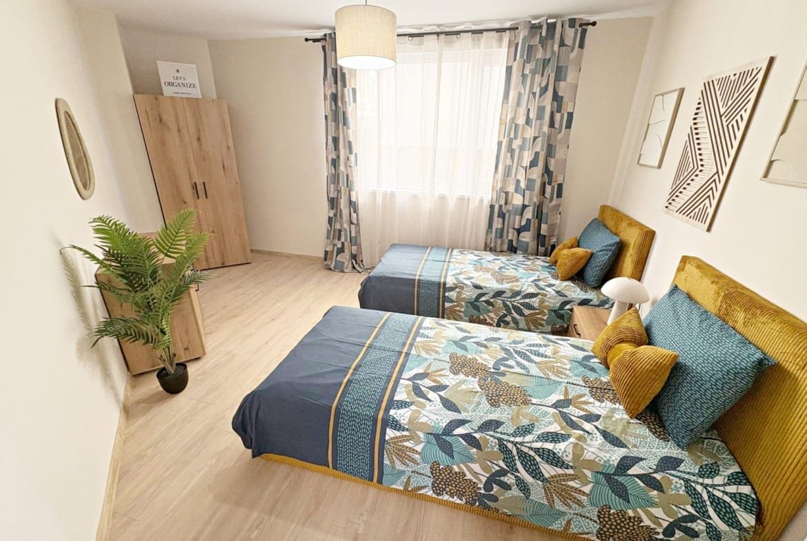 Две кровати с яркими покрывалами, современный интерьер спальни и уютное освещение, идеальные для покупки недвижимости в Болгарии.