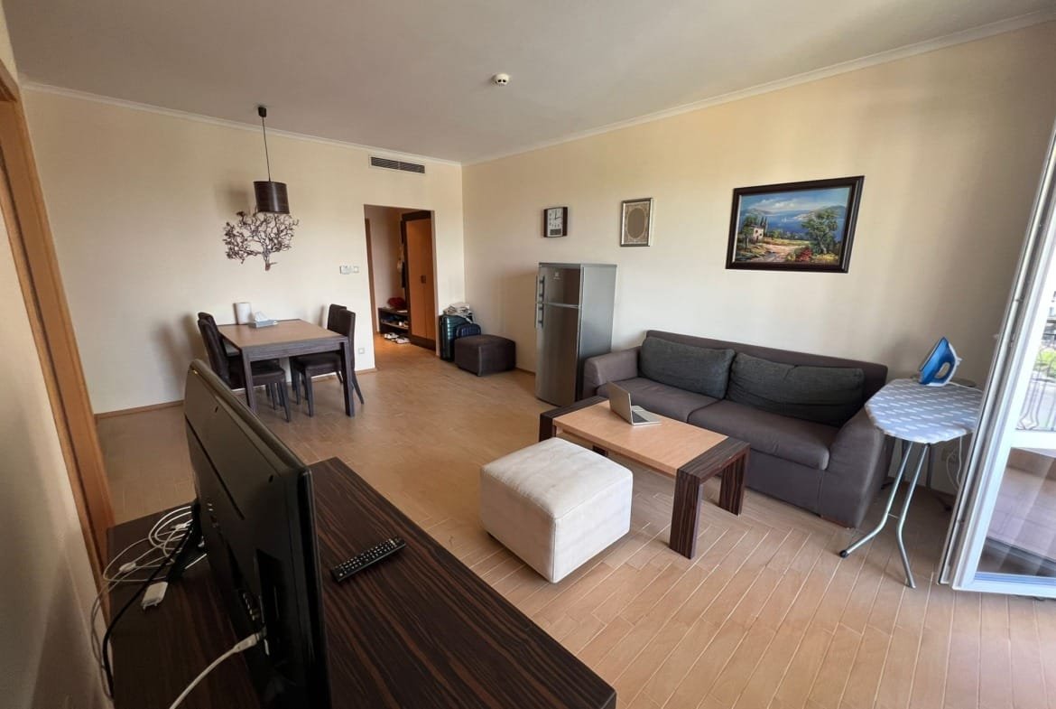 Современная гостиная с диваном, столом и телевизором, идеальное место для отдыха в Болгарии, подходит для покупки недвижимости.