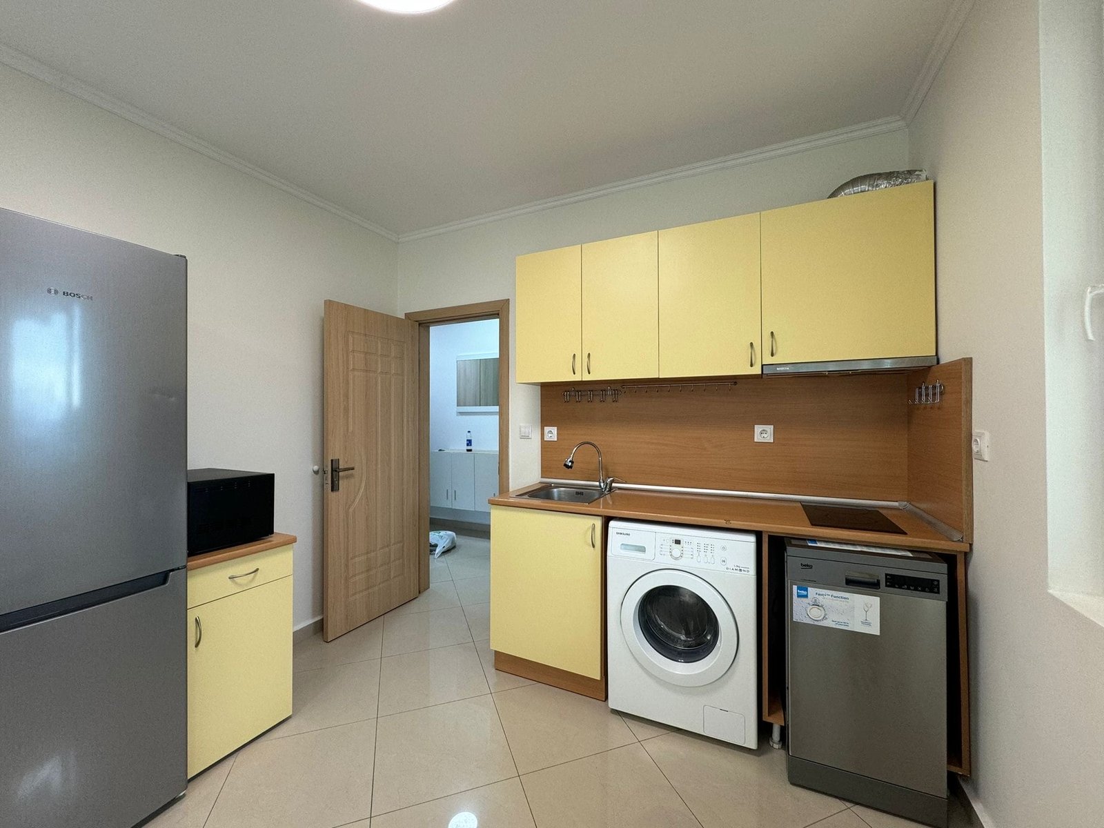 Современная кухня с техникой: холодильник, стиральная машина, посудомойка Современная кухня с жёлтыми шкафчиками, мойкой, стиральной машиной и холодильником в жилом комплексе Болгарии.