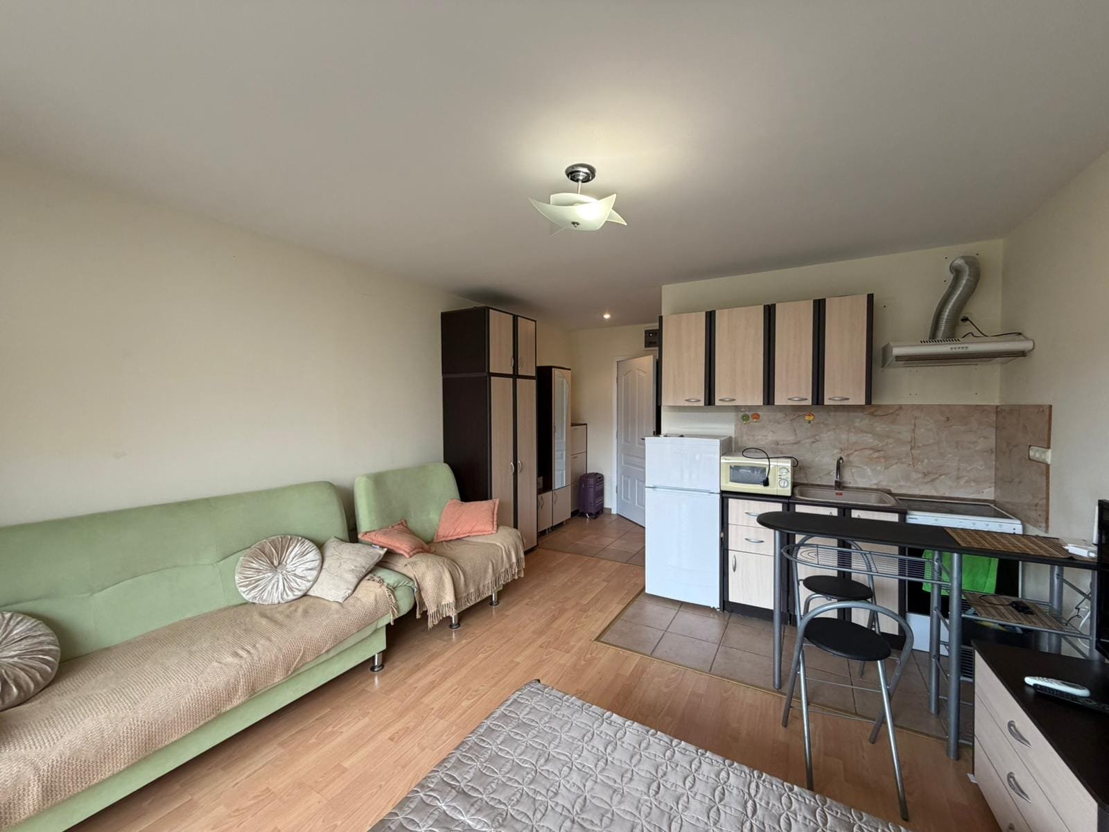 Студия с кухней и мягкой мебелью в светлом интерьере. Современная квартира в Болгарии с кухней, обеденным столом и уютной зоной отдыха, подходит для покупки или аренды.