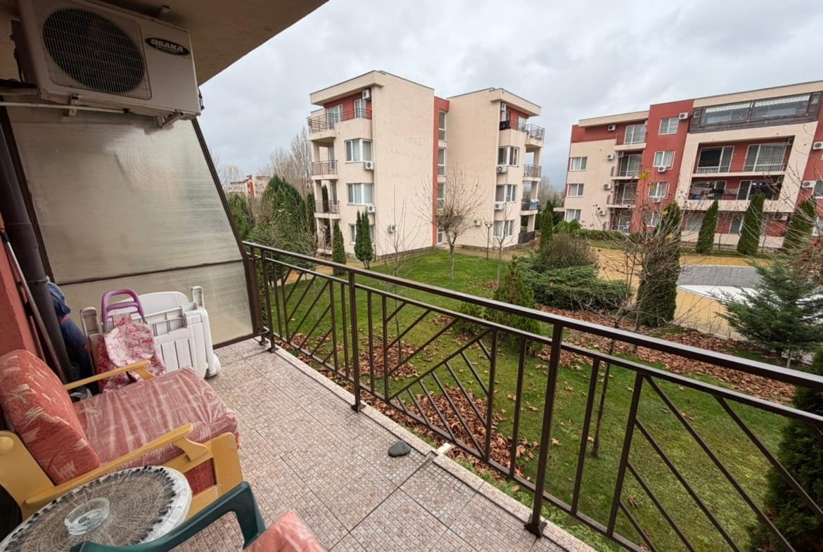 Балкон с видом на зеленую территорию и многоквартирные дома в Болгарии, комфортное место для отдыха и покупки недвижимости.
