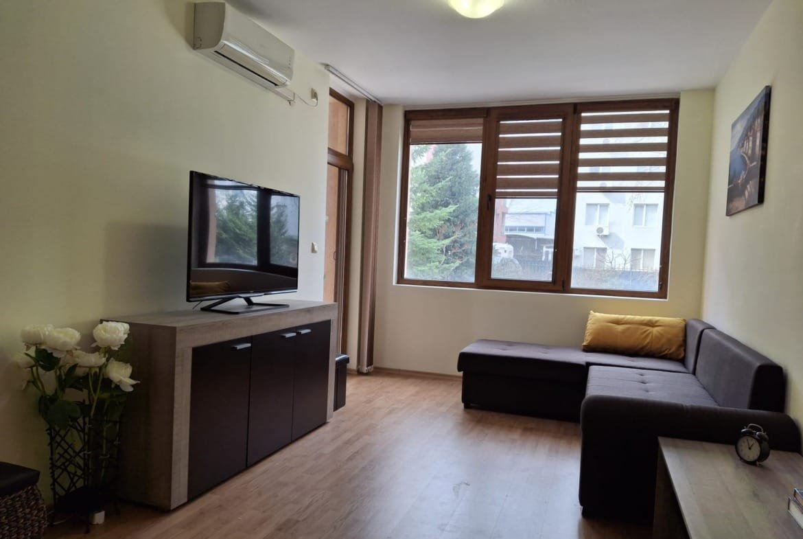 Современный интерьер квартиры с телевизором, диваном, кофейным столиком и большими окнами, излучающими дневной свет.