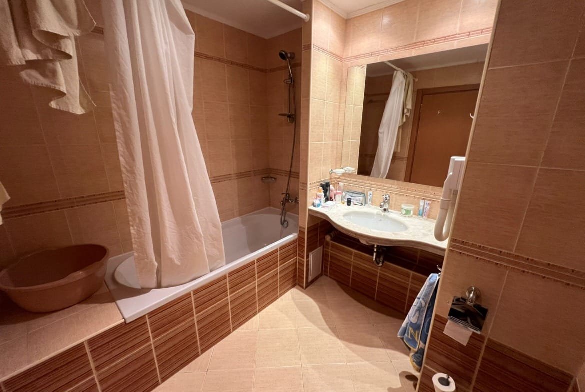 Современная ванная комната с ванной, раковиной и зеркалом, отделанная плиткой в светлых тонах, удобная для жизни в Болгарии.