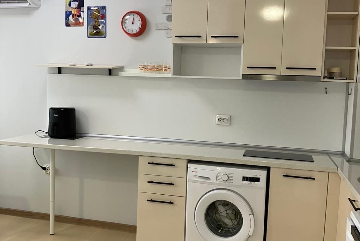 Современная кухня с встроенной техникой, стиральной машиной и функциональными полками, оформленная в светлых тонах.