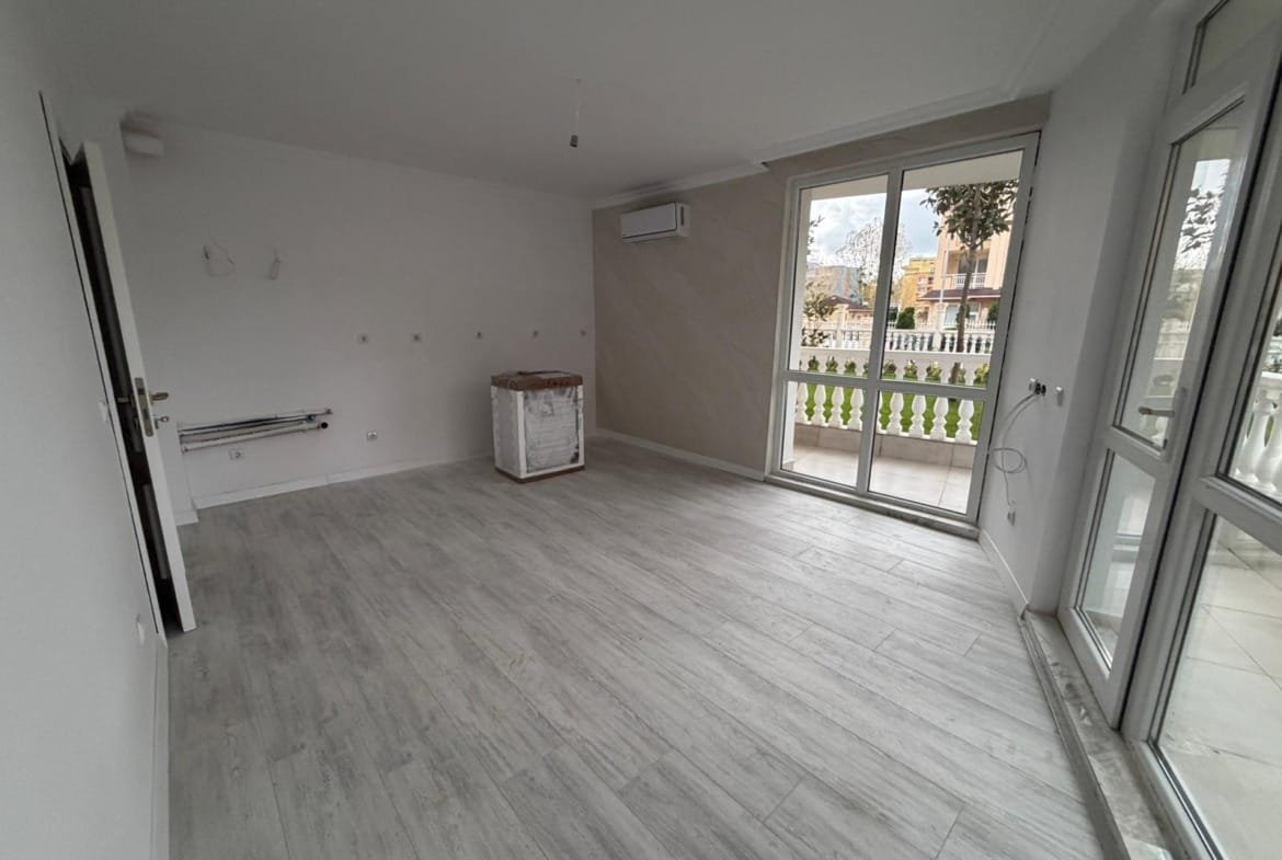 Светлая комната с большими окнами, белыми стенами и деревянным полом, идеальна для покупки недвижимости в Болгарии.