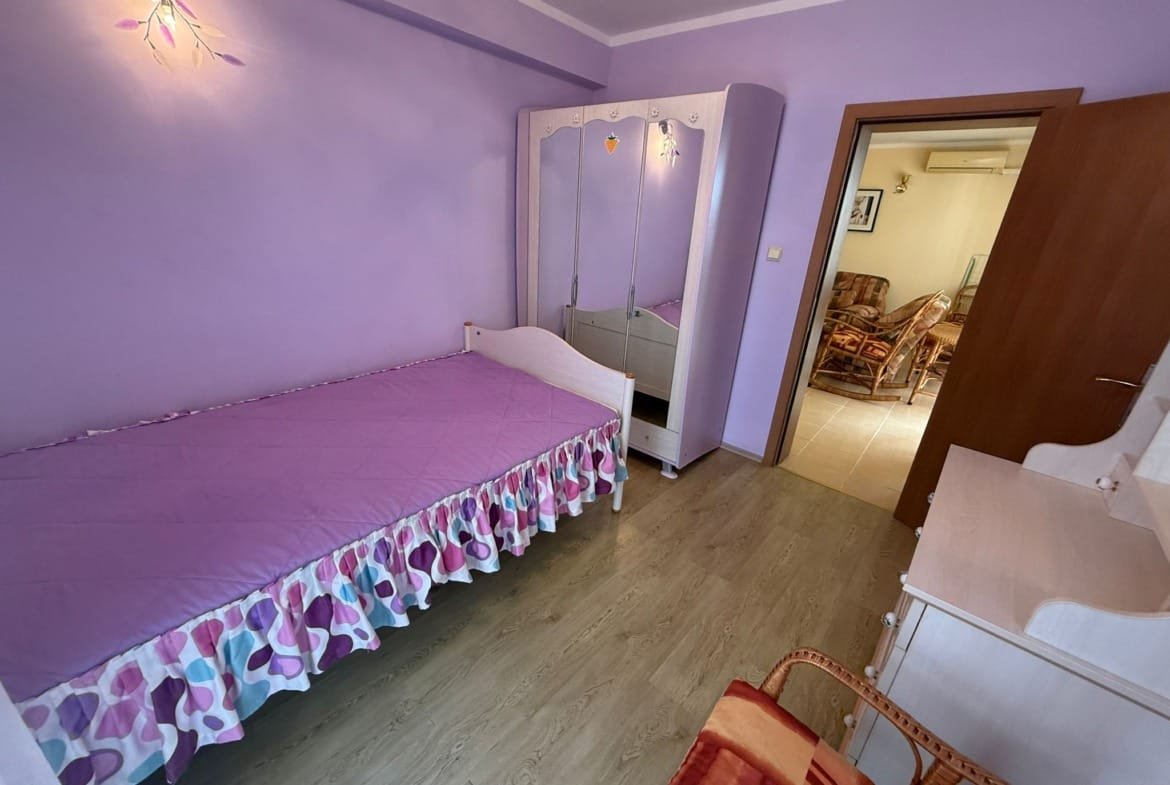 Комната с фиолетовыми стенами, односпальной кроватью и зеркальным шкафом, идеальная для продажи недвижимости в Болгарии.