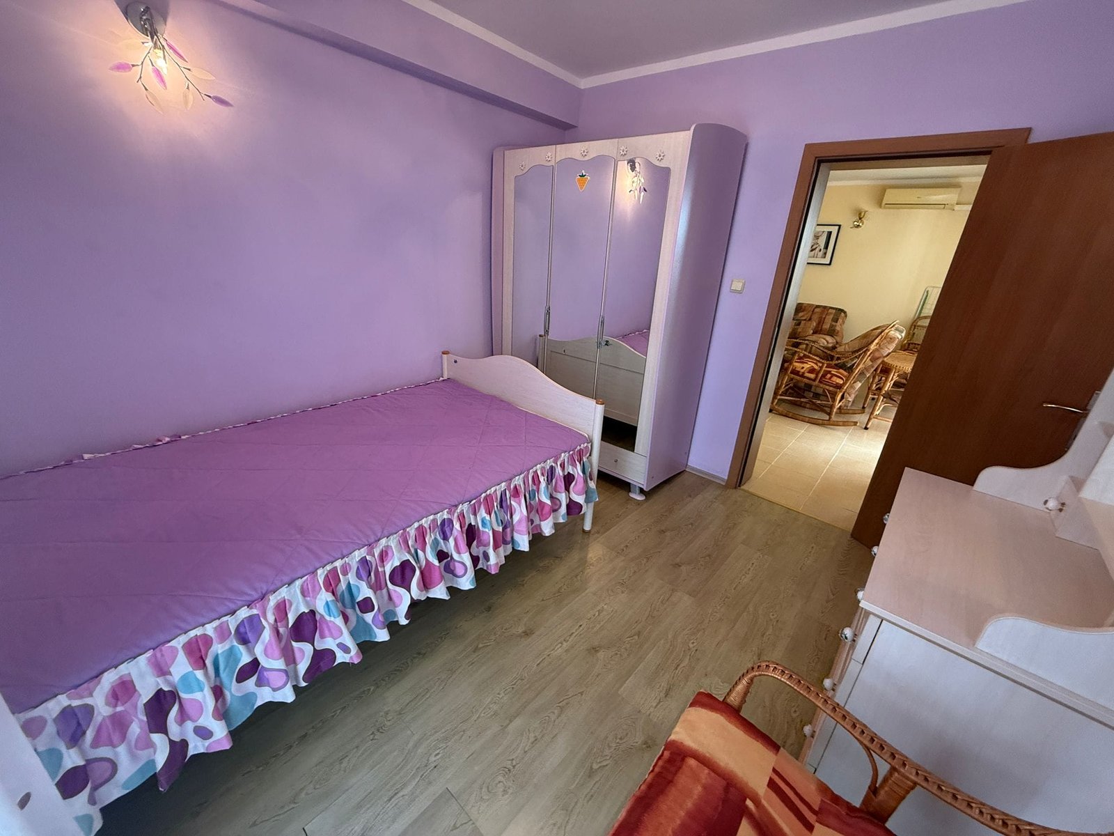 Комната с фиолетовыми стенами, односпальной кроватью и зеркальным шкафом, идеальная для продажи недвижимости в Болгарии.