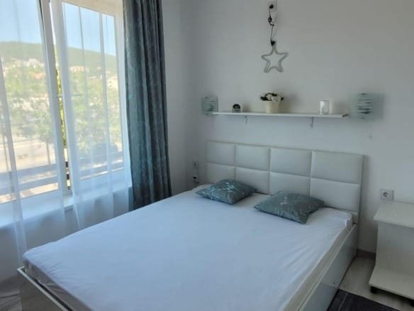 Современная спальня с двуспальной кроватью, светлыми шторами и уютным декором, идеально подходящая для покупки недвижимости в Болгарии.