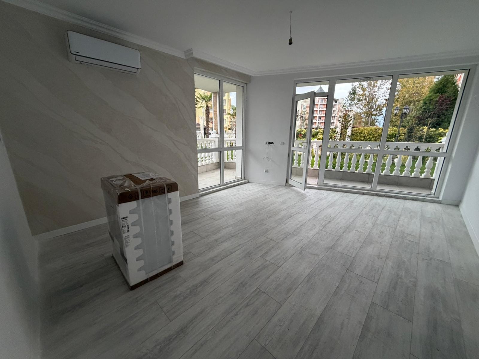 Светлая комната с большим окном, белыми стенами и светлым полом, готовая для продажи недвижимости в Болгарии.