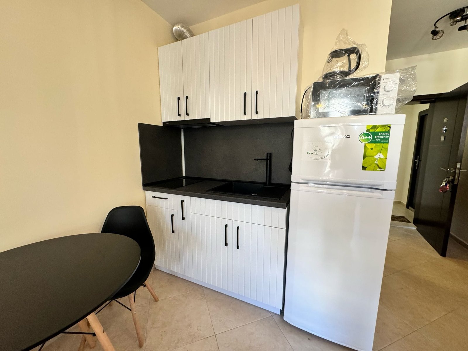 Современная кухня с черной столешницей, белыми шкафами и техникой, идеальная для продажи недвижимости в Болгарии.