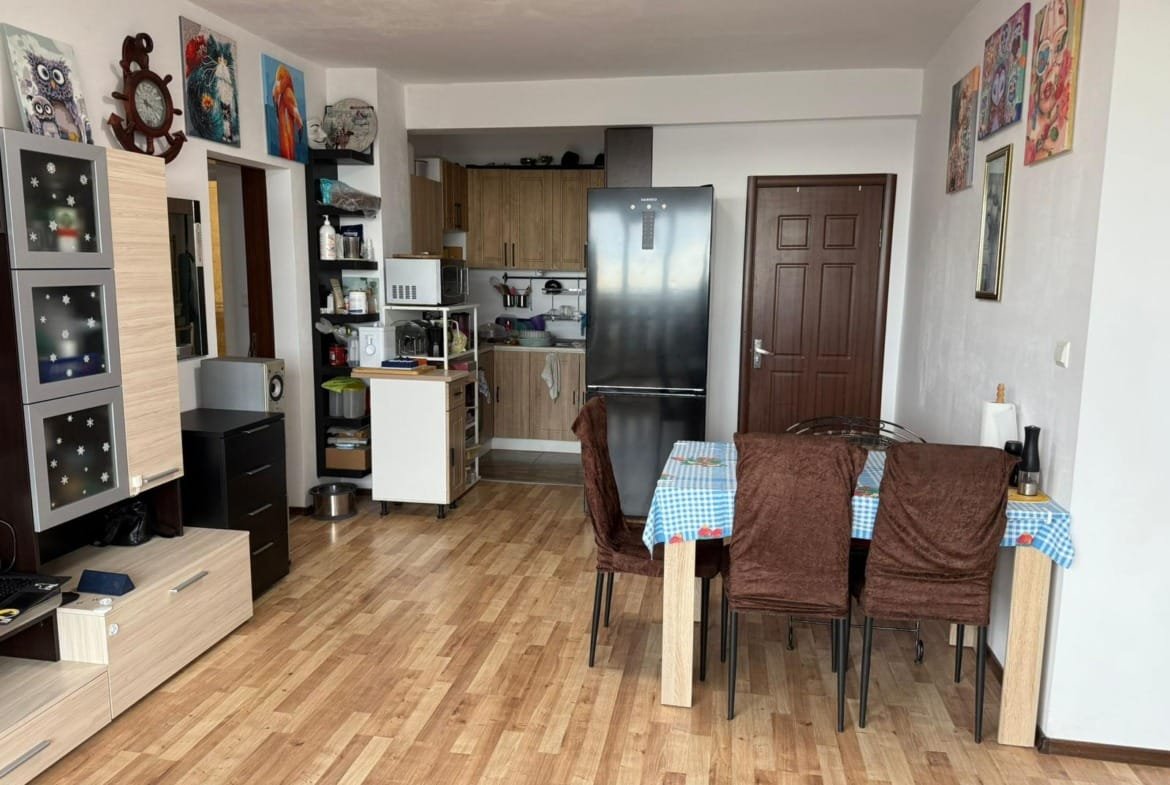 Современная кухня-гостиная с деревянным полом, обеденным столом, холодильником и яркими картинами на стенах в интерьере Болгарии.