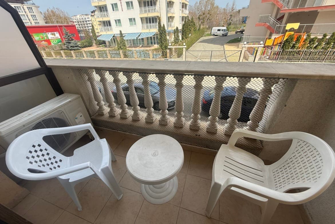 Балкон с двумя пластиковыми стульями и круглым столом, вид на соседние здания, идеальное место для отдыха в Болгарии.