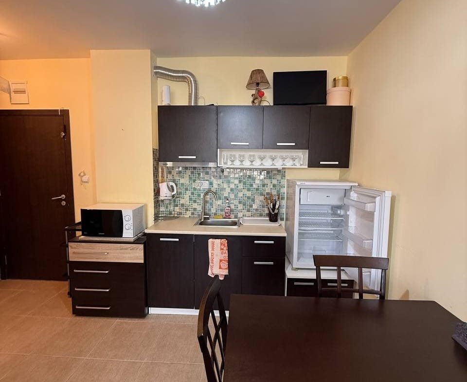 Современная кухня в студии с темными шкафчиками, обеденным столом и бытовой техникой на фоне светло-желтых стен.