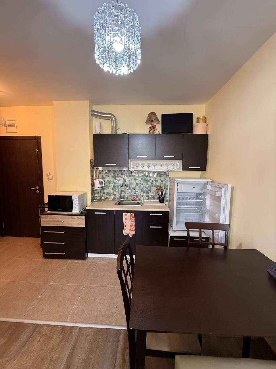 Современная кухня в студии с темными шкафчиками, обеденным столом и бытовой техникой на фоне светло-желтых стен.