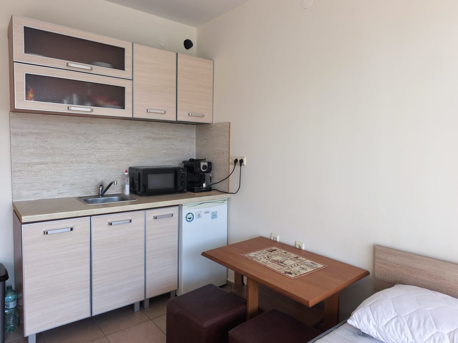 Уютная кухня-студия с бытовой техникой и обеденной зоной Современная кухня с минималистичной мебелью, встроенной техникой и обеденным столом, подходит для жизни в Болгарии.