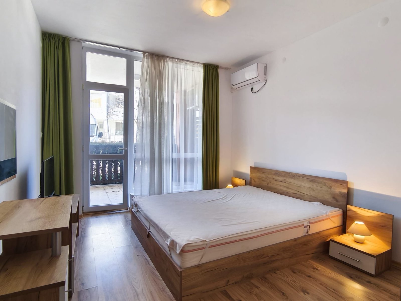 Современная спальня с большими окнами и деревянной мебелью Современная спальня с деревянной мебелью, большими окнами и балконом, идеальная для покупки недвижимости в Болгарии.