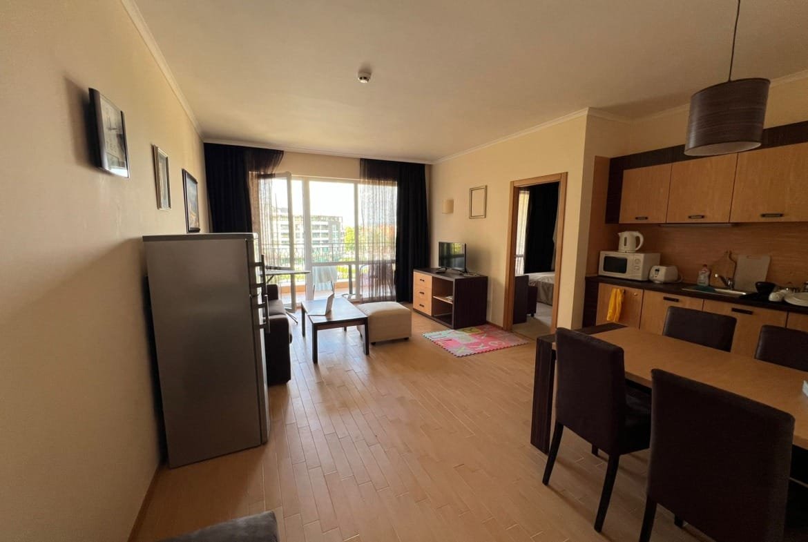 Современная квартира в Болгарии с кухней, обеденным столом и балконом, указывающим на комфорт и уют для покупки или аренды.